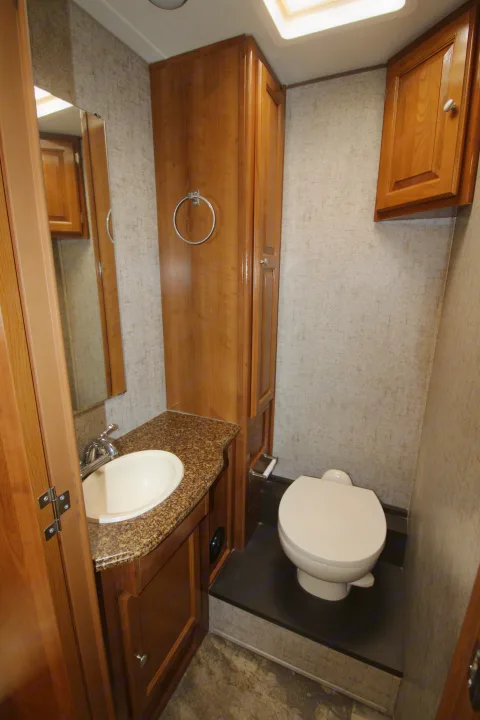 Clean RV rental bathroom featuring a sink, toilet on a raised platform, and wood cabinetry for comfort on the go.. Coachmen Leprechaun 2018