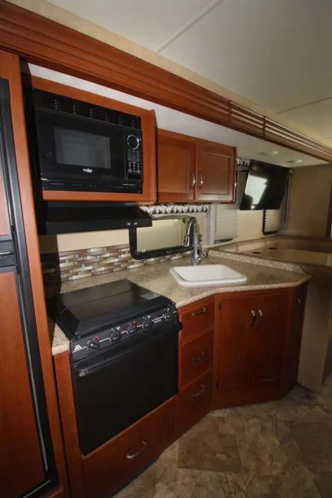 Inside an RV rental, showing a functional kitchen with microwave, stove, sink, and wood cabinets. Great for road trips.. Thor Motor Coach A.C.E 2016