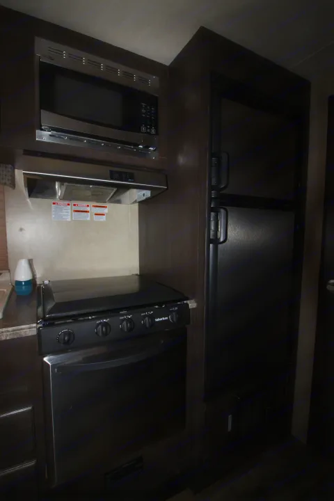 This RV rental features a compact kitchen with dark wood cabinetry, a stainless steel microwave, range, oven, and refrigerator.. Forest River Sonoma 2017