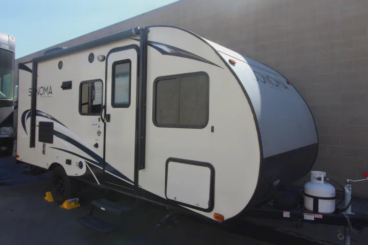 This RV rental features a white Sonoma travel trailer with an awning, propane tank, and steps, parked outdoors by a brick wall.. Forest River Sonoma 2017