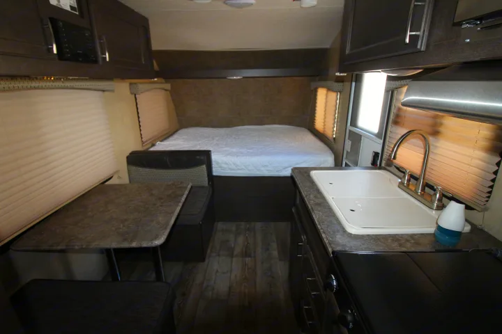 This RV rental interior showcases a full bed, dinette, and kitchen with a sink and stovetop, offering comfort for travel.. Forest River Sonoma 2017