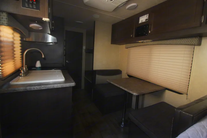 Cozy RV rental interior featuring a compact kitchen with sink and a comfortable dinette with bench seating and overhead cabinets.. Forest River Sonoma 2017