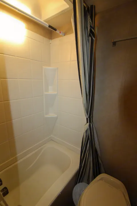 Compact RV rental bathroom: white tiled shower, bathtub, striped curtain, and a portion of the toilet.. Forest River Sonoma 2017