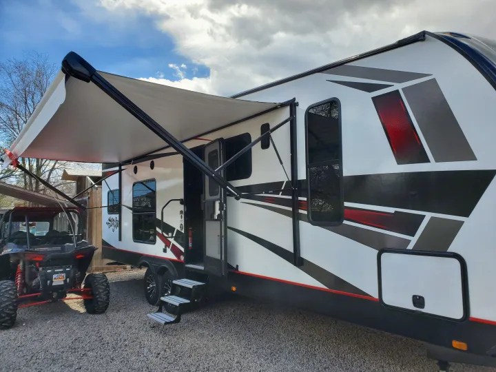 RV rental: Modern white toy hauler camper with awning extended, an ATV beside it on gravel. Your adventure begins!. Cruiser Rv Corp Stryker 2020