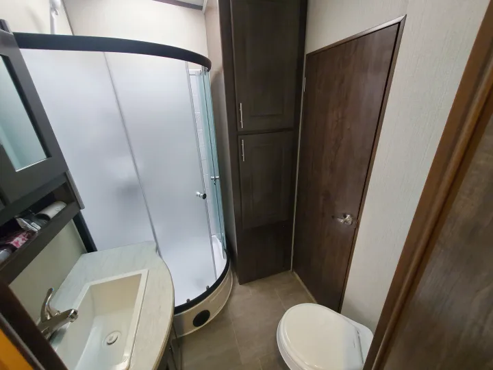 This RV rental bathroom features a curved shower, sink, toilet, and dark wood cabinets, offering compact utility.. Cruiser Rv Corp Stryker 2020