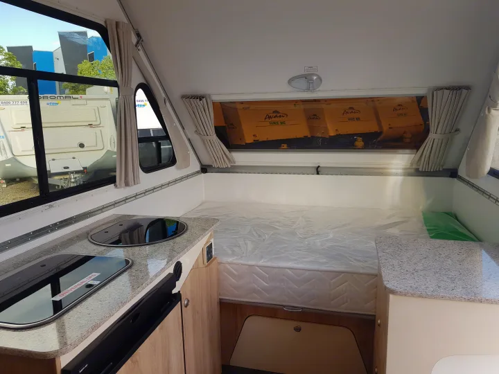 Compact RV interior, showing kitchen and bed. Exterior signs advertise "Avan HIRE ME", indicating an RV rental available.. Avan Aliner Camper 2022