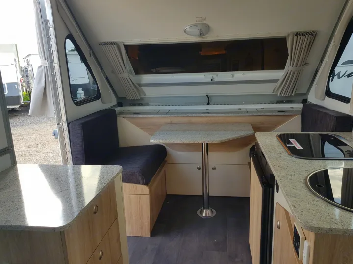 Interior of an RV rental showing a compact dining area with a table and bench, plus a small kitchen counter.. Avan Aliner Camper 2022