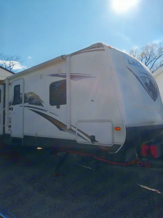 Bright sun shines on this white Laredo Luxury Lite RV, ideal for an rv rental. It's parked outdoors under a blue sky.. Prime Time Lacrosse 2013