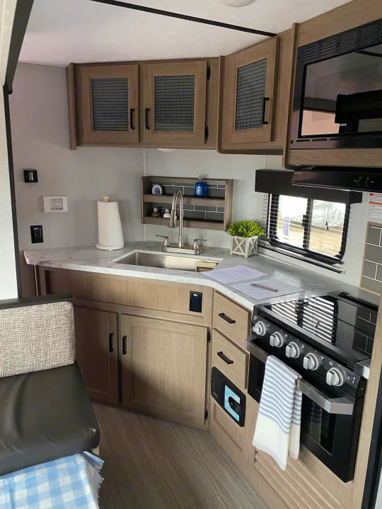 Compact RV rental kitchen with modern wood cabinets, grey countertops, sink, stove, and microwave, perfect for travel.. Keystone Hideout 2020