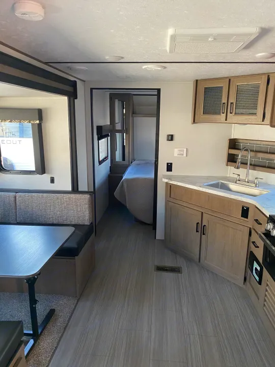 Inside a modern rv rental: full kitchen, dining booth, and private bedroom with a bed.. Keystone Hideout 2020