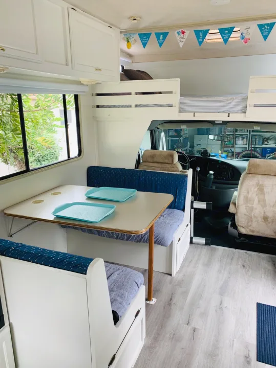 Bright RV rental interior: dining area with blue cushions, overhead bunks, and driver's cab.. Itasca Spirit 1999