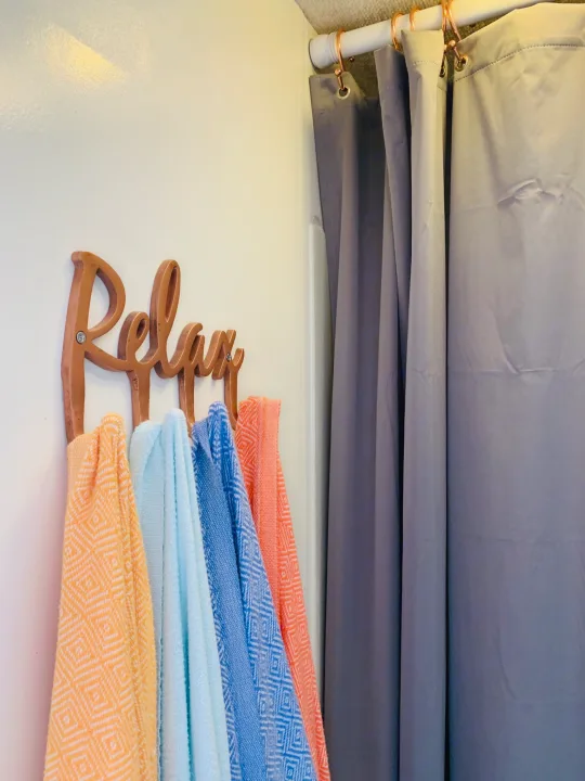 Inviting RV rental interior: 'Relax' sign holds colorful towels beside gray shower curtain. Enjoy your trip!. Itasca Spirit 1999