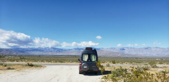 Explore stunning desert landscapes! This RV rental van is parked on a dirt road, facing snowy mountains under a blue sky.. ERA Era 2010