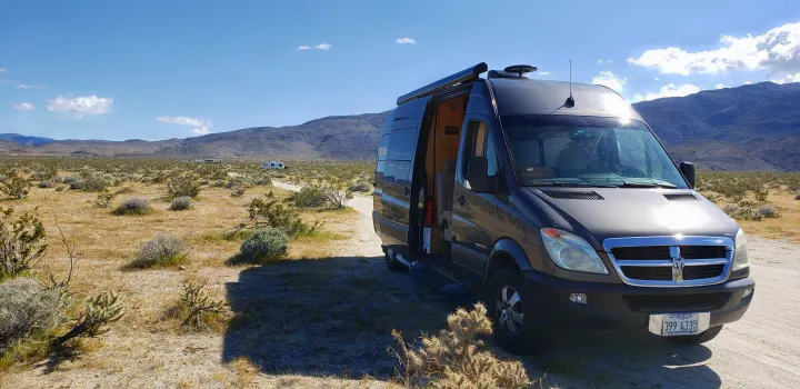 Dark gray RV rental van parked in a sunny desert with mountains and other RVs in the distance on a dirt road.. ERA Era 2010