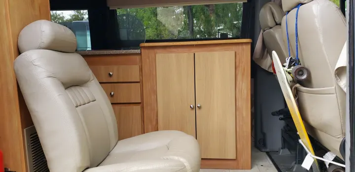 RV rental interior: tan captain's chair, wood cabinets, window view, and a skateboard hanging from a seat.. ERA Era 2010