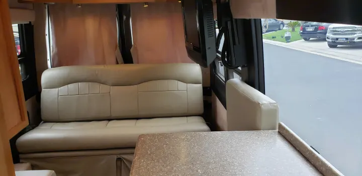 Relax in this RV rental's cozy interior, featuring a plush sofa, dining table, and TV, with a view of the road outside.. ERA Era 2010