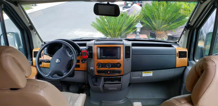 RV rental cockpit featuring a wood-grain dash, brown seats, and a view of the street and palm trees.. ERA Era 2010