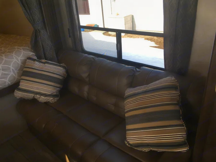 Cozy RV rental interior with a brown sofa, striped pillows, and window view showing snow, ready for relaxing travel.. Forest River Cherokee Grey Wolf 2018