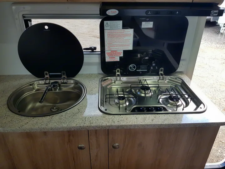 RV rental kitchen with open glass covers on a sink and 3-burner stove, perfect for compact camper cooking.. Avan Aspire 499 Bunk 2020