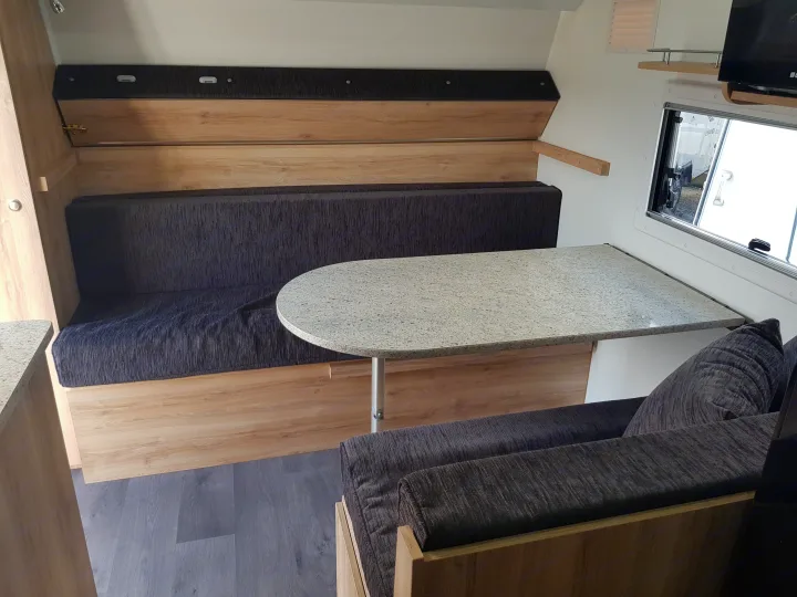 Cozy RV rental interior: a compact dinette with dark grey cushioned seating, light wood walls, and a speckled table.. Avan Aspire 499 Bunk 2020