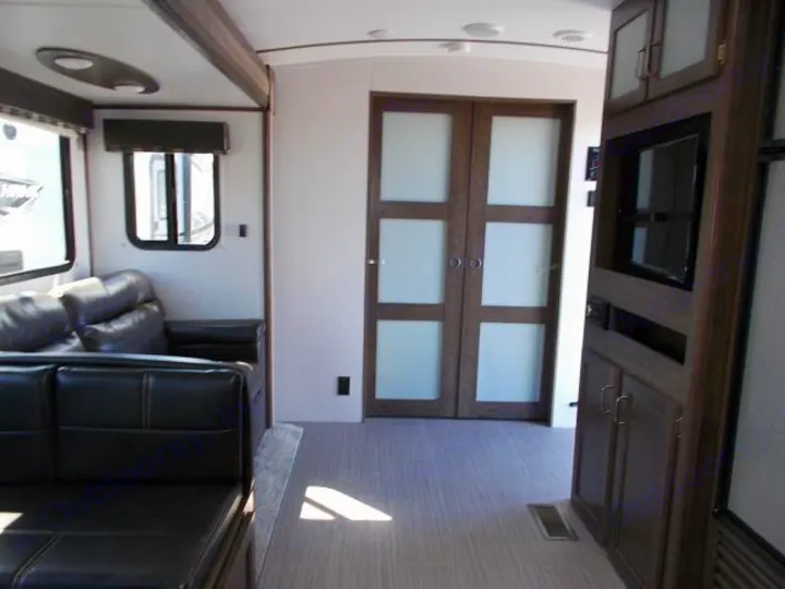 This inviting RV rental interior features a cozy leather sofa, entertainment center, and stylish frosted glass doors, perfect for travel.. Keystone Passport 2020