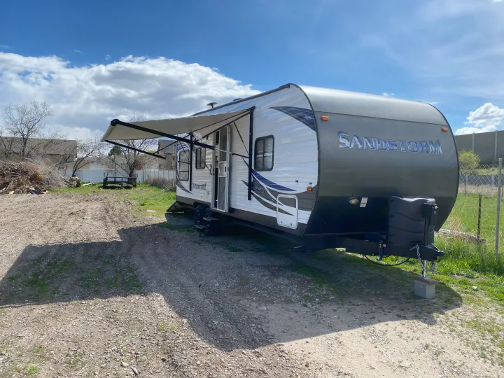 Sandstorm travel trailer RV rental with awning extended, parked on a gravel lot under a blue sky.. Forest River Sandstorm 2017
