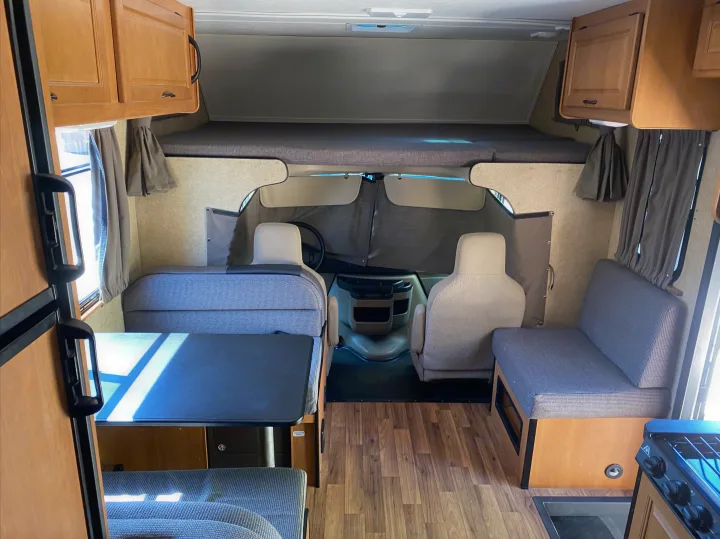 Spacious RV rental interior: wood-look floor, light cabinets, dinette, cab-over bunk, and driver's area.. Thor Motor Coach Four Winds Majestic 2015
