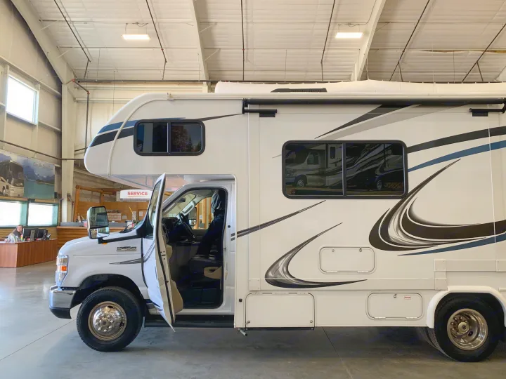 Large white RV rental parked indoors at a dealership, driver's door open.. Forest River Sunseeker 2019