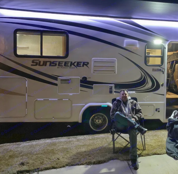 Enjoying a relaxed evening by an RV rental. A man sits outside a brightly lit Sunseeker motorhome at night.. Forest River Sunseeker 2019
