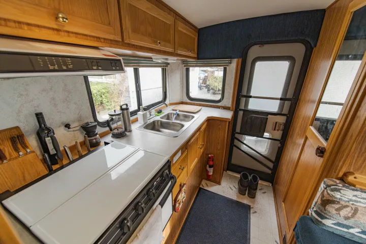 Spacious RV rental kitchen featuring a double sink, stovetop, wooden cabinets, and windows with outdoor views.. Ford Other 1996