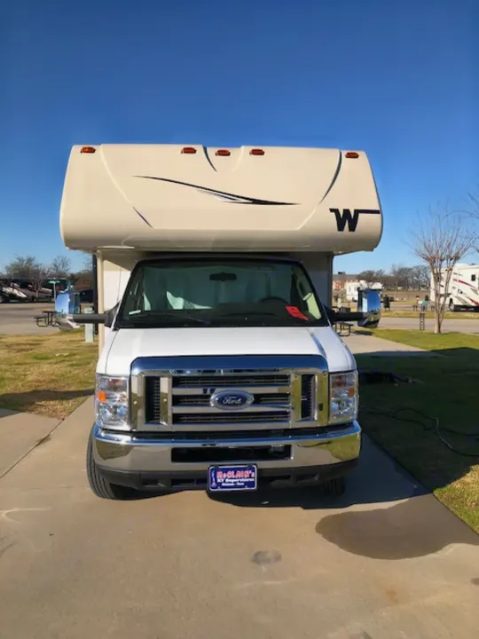 A white Winnebago Ford Class C motorhome, parked on an asphalt lot under a blue sky, available for rv rental.. Winnebago Minnie Winnie 2020