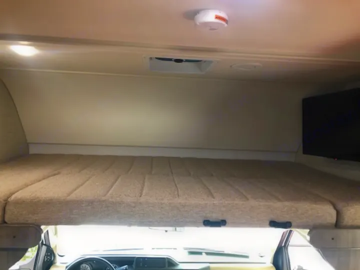 Cozy cab-over bunk in an RV rental, featuring a mattress, TV, light, and smoke alarm. Perfect for road trip adventures.. Winnebago Minnie Winnie 2020