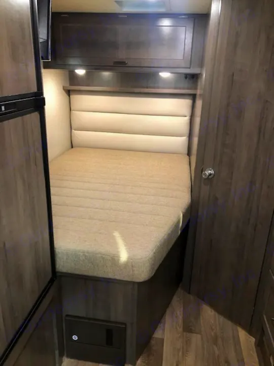 Modern RV rental bedroom with a comfortable bed, light padded headboard, and dark wood storage/cabinets.. Winnebago Minnie Winnie 2020