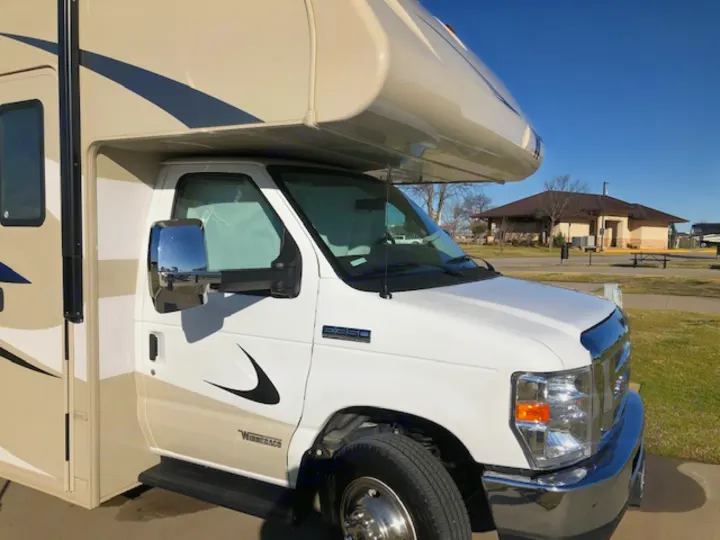 View of a clean white and tan Winnebago RV rental, parked on a sunny day with a building and picnic area in the background.. Winnebago Minnie Winnie 2020