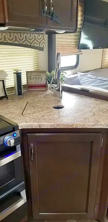 Compact RV rental kitchen features a modern sink, faucet, oven, dark cabinets, and a glimpse of the bedroom.. Other Other 2020