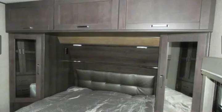 RV rental bedroom: Dark gray bed with padded headboard, overhead storage, and mirrored wardrobes on each side.. Grand Design Reflection 2019