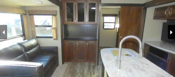Inside a modern **rv rental** living area: a black sofa, wood-look cabinets, and a kitchen island with a sink. Bright and functional space.. Grand Design Reflection 2019