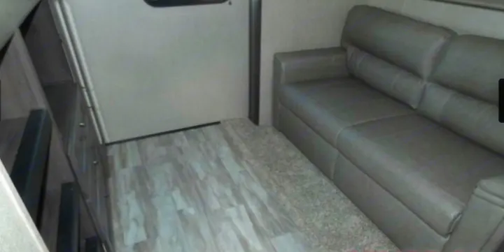 RV rental interior: A cozy living space featuring a gray leather sofa, wood-look flooring, and built-in storage.. Grand Design Reflection 2019