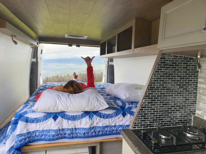 Cozy RV rental interior: A person relaxes on a bed, enjoying panoramic mountain views from open back doors. Features a kitchenette.. Dodge Sprinter 2500 170ext 2015