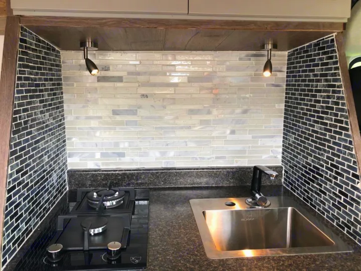Compact RV rental kitchen with sleek stove, sink, and striking gray/black tile backsplash. Perfect for on-the-go cooking.. Dodge Sprinter 2500 170ext 2015