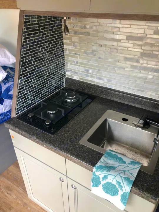 Clearly shows an RV rental's compact kitchen. Features a dual-burner stovetop, sink, dark countertop, and mosaic tile backsplash.. Dodge Sprinter 2500 170ext 2015