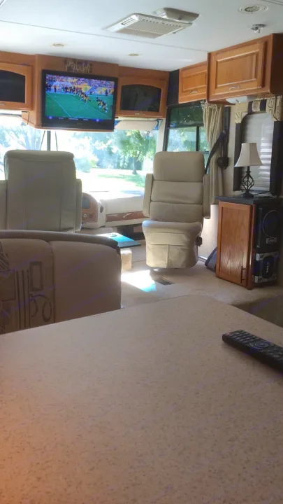 Inside an RV rental: a spacious living area with a TV playing football, plush front seats, and wooden cabinetry.. Thor Motor Coach Hurricane 34N 2006