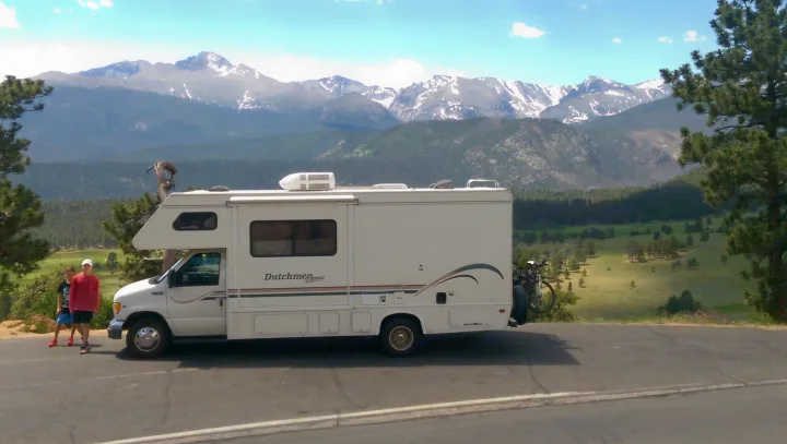 Scenic rv rental journey: a white Dutchmen Express motorhome parked with two travelers and stunning snow-capped mountains.. Dutchmen Other 2001