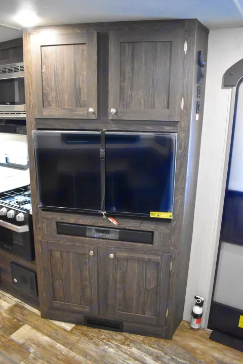 RV rental living space: dark wood cabinets, TV, and soundbar are central. Kitchen appliances and an entry door are also visible.. Starcraft Travel Trailer 2020
