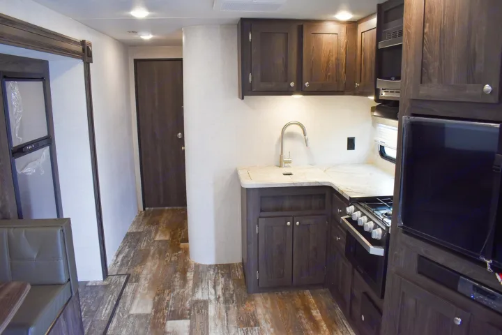 RV rental's modern interior with dark wood kitchen cabinets, light counter, sink, stove, and a dining bench.. Starcraft Travel Trailer 2020
