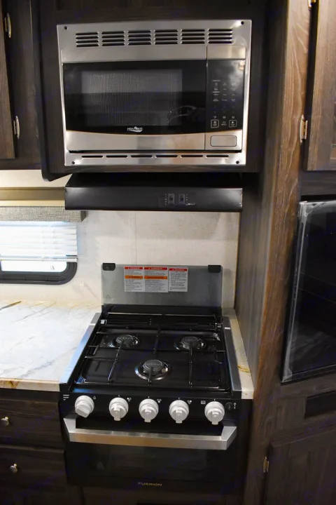 RV rental kitchen features a stainless steel microwave, range hood, and black Furrion gas stove with oven, perfect for your trip.. Starcraft Travel Trailer 2020