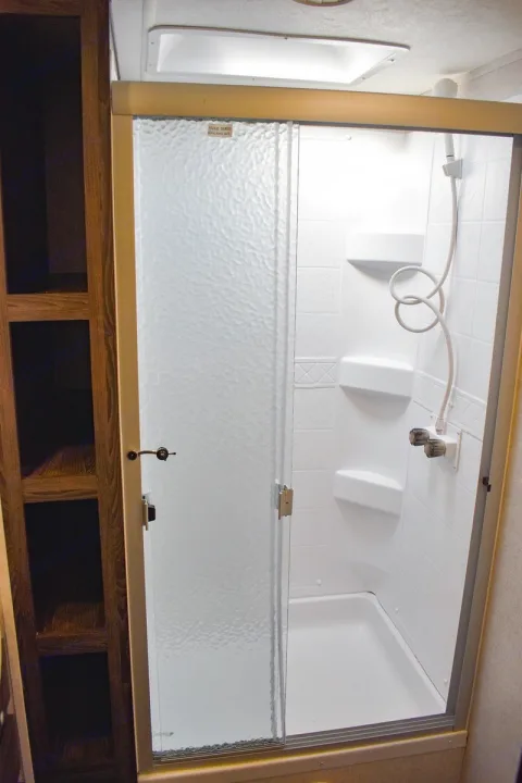RV rental shower: compact design with textured sliding glass door, built-in shelves, handheld shower, and bright interior light.. Starcraft Travel Trailer 2020