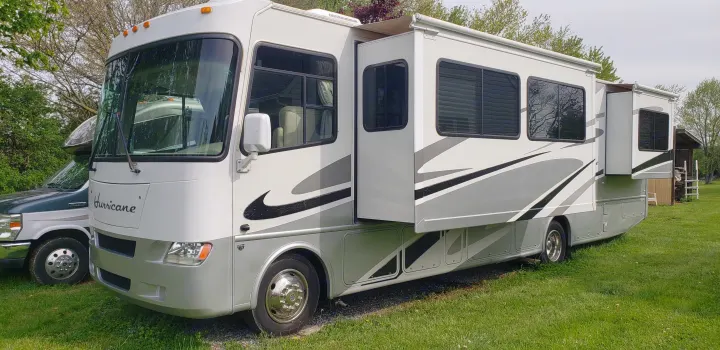 A white and gray Class A Hurricane RV with slide-outs extended, parked on grass. Explore options for your rv rental trip!. Thor Motor Coach Hurricane 34N 2006