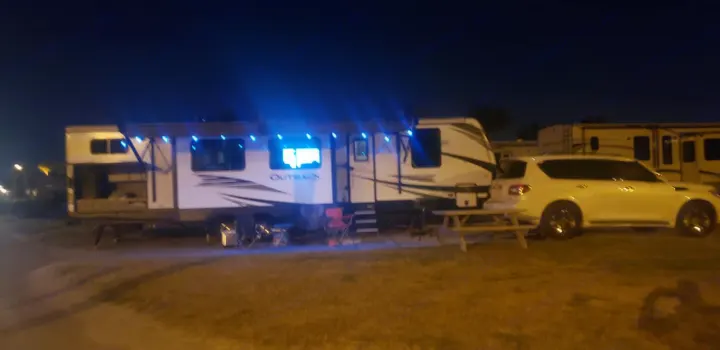 Night at an RV park: A brightly lit white travel trailer, SUV, and picnic setup, ideal for an RV rental.. Keystone Outback 2020