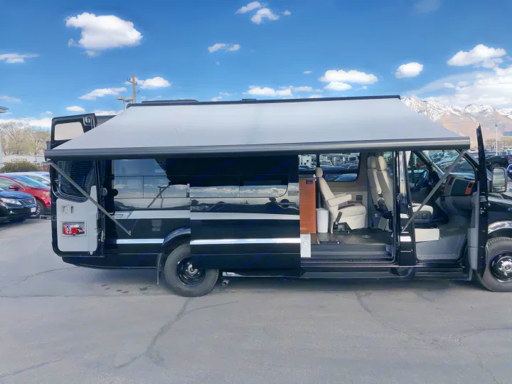 Spacious black camper van with open side door & extended awning, mountains backdrop. Discover your next rv rental adventure!. Winnebago Era 2014